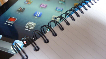 An ipad half-visible under a notepad.