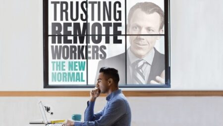 Person on laptop sits in front of sign reading 'trusting remote workers, the new normal'