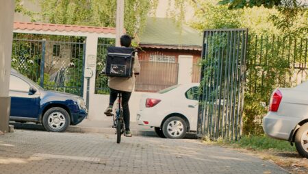 woman working as takeaway courier riding bicycle on street