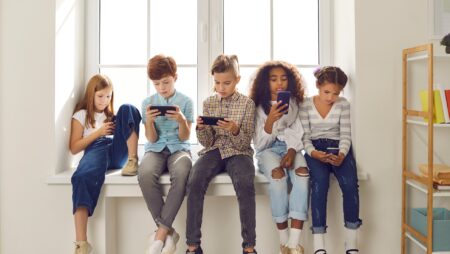 A group of children sit together looking at mobile phones