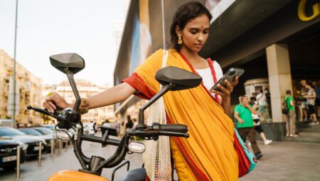 Young Indian woman using mobile phone while standing with scooter outdoors